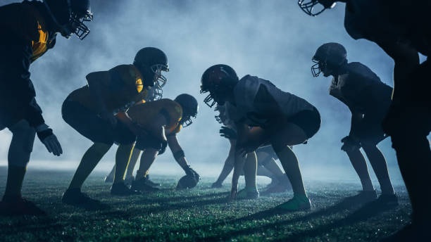 American Football Field Two Teams Stand Opposite Each Other, Ready to Start the Game. Professional Athletes Ready to Compete for the Ball and Fight for Victory. Dramatic Blue Night Fog